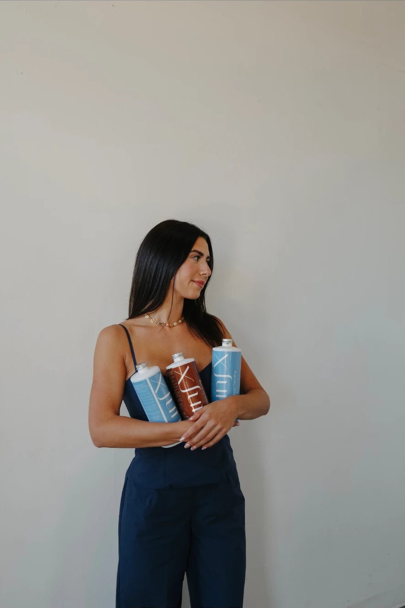 A woman with tanned skin holding three sunless tanning bottles